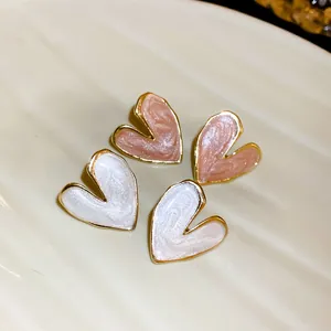 Close-up detail of small heart-shaped stud earrings in pearl white and soft pink enamel