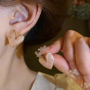 Close-up detail of elegant pink drip oil heart stud earrings with golden trim on model's ear
