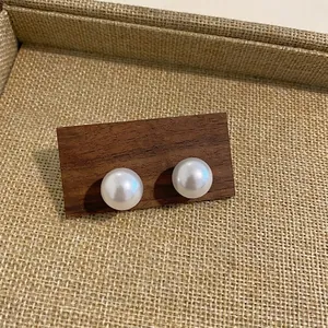 Close-up of elegant white pearl stud earrings with a lustrous finish on a wooden base.