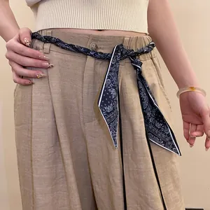 Detailed view of a navy blue patterned silk scarf woven belt styled on linen trousers