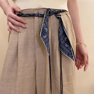 Detail of a chic Paisley silk scarf woven waist chain on beige linen trousers.