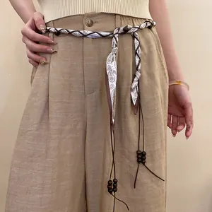 Close-up of a woven silk scarf waist chain featuring paisley patterns and wooden beads.