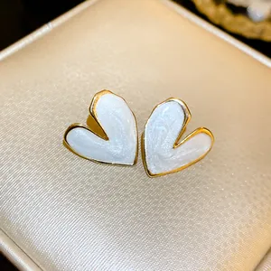 Close-up of heart-shaped gold-toned earrings with white pearlescent enamel finish