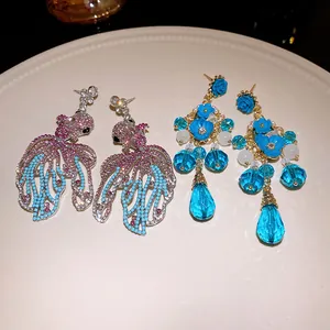 Primo piano di orecchini pendenti a forma di pesce rosso e fiori blu scintillanti