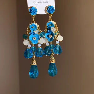 Dettaglio macro di orecchini a lampadario a fiori blu con cristalli e dettagli oro.