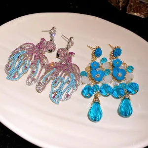 Dettaglio orecchini a pesce con strass e ciondoli a fiore blu in cristallo su un piatto.