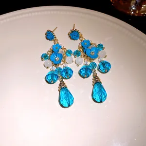 Dettaglio ravvicinato di orecchini pendenti con fiori blu e cristalli dorati