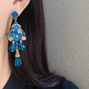 Dettaglio di eleganti orecchini pendenti con fiori blu e ciondoli di cristallo a goccia