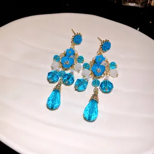 Primo piano di eleganti orecchini pendenti con fiori in cristallo blu su vassoio