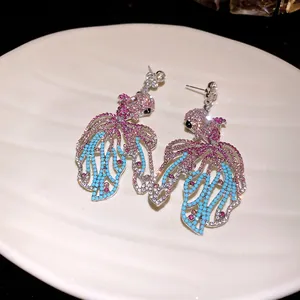 Vista dettagliata degli orecchini a forma di pesce con strass rosa e blu su piatto.