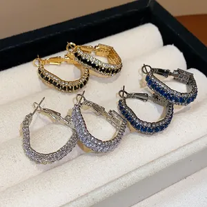 Close-up view of geometric zircon hoop earrings in gold, silver, and blue colors.