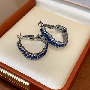 Close-up of geometric silver hoop earrings with blue and white zircons in a jewelry box.