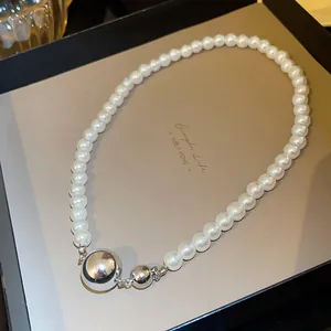 Detail of pearl necklace featuring two polished silver spheres on a beige display