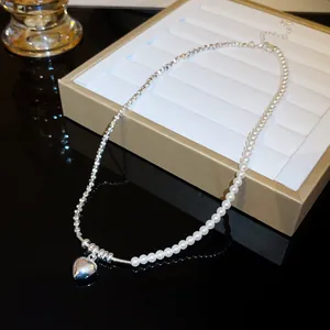 Macro detail of a silver heart pendant on a stylish pearl and metal link chain necklace