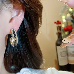 Macro detail of elegant gold-toned hoop earrings inlaid with black zircons on ear