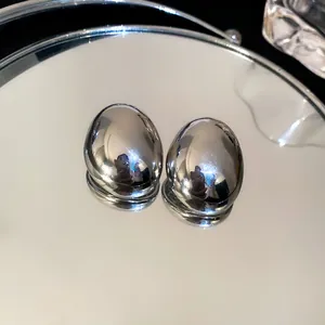 Detalle de pendientes de botón ovalados irregulares con acabado metálico plateado brillante
