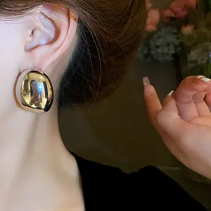 Primer plano de pendientes de metal ovalados irregulares usados por una modelo en sombra