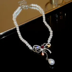 Macro view of bow pendant necklace featuring pearls and red heart gemstone.