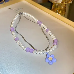 Close-up of double-layered pearl necklace with a purple flower pendant and snake chain.