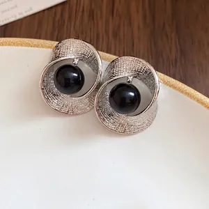 Silver twisted pleated earrings with black bead on a white plate