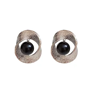 Elegant twisted silver texture stud earrings with a central black bead on a white background
