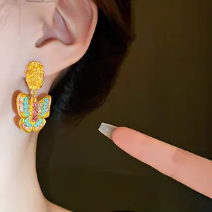 Close-up of a gold butterfly earring with pink and blue rhinestones on an ear.