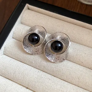 Detailed view of silver textured pleated earrings with central black beads in a display box