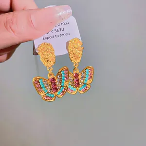 Close-up of gold butterfly earrings with colorful rhinestones and textured metal design.