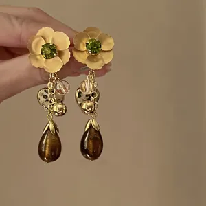Detail shot of pleated metal flower earrings with green gemstone and tassel charms