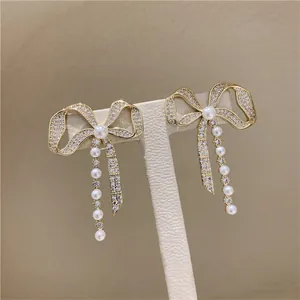 Elegant bow-shaped stud earrings with pavé diamonds and dangling pearl drops.