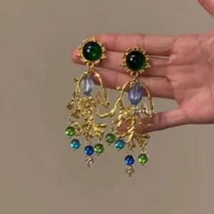 Macro view of ornate vintage gold drop earrings featuring vibrant green and blue gemstones