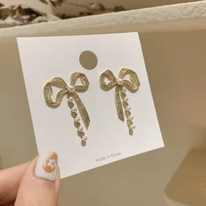 Detailed view of elegant gold bow earrings featuring rhinestones and dangling pearls