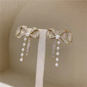 Close-up of elegant gold bow earrings with sparkling rhinestones and delicate white pearls
