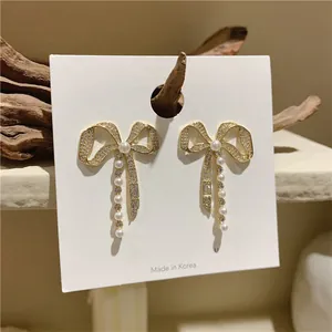 Close-up of elegant silver needle bowknot earrings decorated with rhinestones and pearls