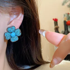 Close-up detail of a vintage turquoise flower stud earring with intricate beadwork on an ear