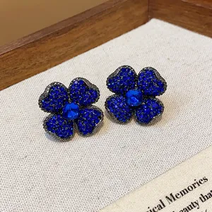 Close-up view of elegant vintage-style four-petal flower stud earrings with blue rhinestones