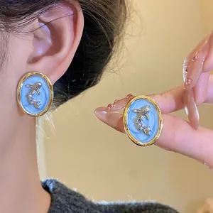 Detailed view of vintage oval earrings featuring blue enamel and silver fish motif.