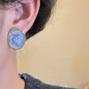 Close-up of vintage oval goldfish earring with pearl accents and blue enamel detail