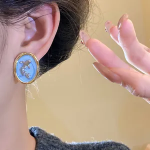 Close-up of vintage oval earring featuring goldfish and pearl details on blue background