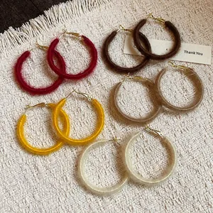 Detail of autumn winter woven fabric hoop earrings in multiple colors on a textured rug.