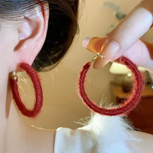 Close-up of red woven hoop earrings featuring cozy braided fabric texture for autumn