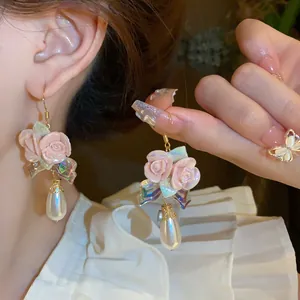 Close-up of pink ceramic flower earrings with iridescent bows and teardrop pearls.