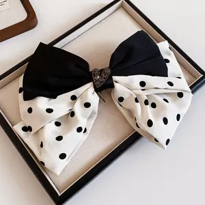 Detail of a black and white polka dot fabric bow hair clip with a crystal heart center.