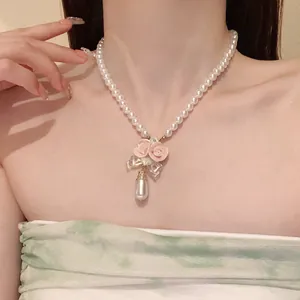 Close-up of elegant pearl necklace with pink ceramic roses and teardrop pendant on model