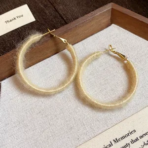 Close-up of beige fabric-wrapped hoop earrings on a textured fabric background.