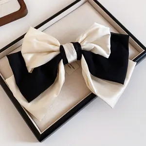 Elegant black and cream fabric bow hair clip with smooth satin texture in display tray