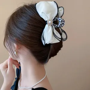 Elegant white fabric bow hair claw clip with pearl center shown on brown styled hair
