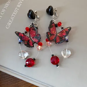 Close-up of red butterfly dangle earrings with beads and black heart studs