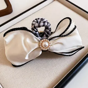Detailed view of elegant cream fabric bow hair claw clip with central pearl and black piping