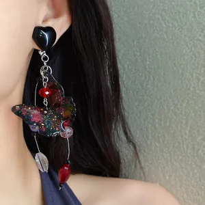 Detailed shot of dark butterfly drop earrings with heart stud and starry glitter wing design